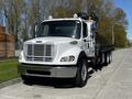 A white 2012 Freightliner M2 112 flatbed truck with a prominent grille and reflective lights parked on a street