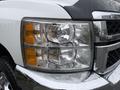 Close-up of the front headlight of a 2013 Chevrolet Silverado 3500HD with visible raindrops on the surface and a shiny chrome finish