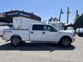 A white 2014 Ford F-150 pickup truck is parked with its driver side facing the viewer showcasing its cab and bed design