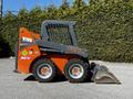A 2017 Gehl R105 skid steer loader with a black and orange exterior featuring a bucket attachment and large wheels