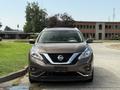 A 2016 Nissan Murano with a brown exterior is parked facing forward with its headlights on and a chrome grille visible