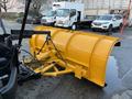 A yellow snow plow attachment with a curved design and chains is mounted on the front of a truck preparing for snow removal