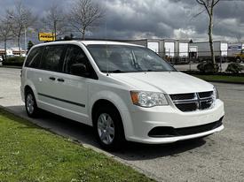 A white 2011 Dodge Grand Caravan parked with a sliding side door visible and a front view showcasing its distinctive grille and headlights