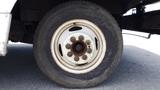 A close-up view of a rusty white steel wheel from a 2011 Ford Econoline with a worn tire and visible lug nuts