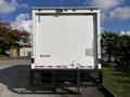 A white 2016 Isuzu NPR delivery truck viewed from the rear with a closed roll-up door and a hitch attachment at the bottom