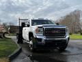 A white 2017 GMC Sierra 3500HD with a flatbed and a black mesh rear panel parked on a paved surface