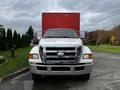 A white 2008 Ford F-750 truck with a silver grille and chrome bumper facing forward with a large red cargo container in the background