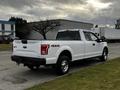 A white 2016 Ford F-150 pickup truck is parked with its rear facing the viewer showcasing its four-wheel drive and chrome wheels