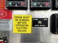 A control panel featuring buttons and switches with a cautionary yellow sign stating engine must be running before operating electric valves and a switch labeled aerial nozzle