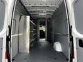 A 2023 Mercedes-Benz Sprinter van with an empty interior featuring metal shelving on the sides and a spacious cargo area with a clean floor
