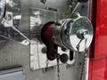 Close-up of a chrome fire hose connection on a red fire truck with a pull chain for draining and an inlet labeled in bold letters