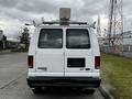 A white 2011 Ford Econoline van with a roof rack and equipment mounted on top viewed from the rear