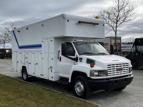 A 2006 GMC C5000 truck with a white exterior featuring blue stripes and multiple storage compartments on the sides