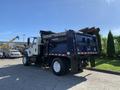 A white 2007 International 7300 truck with a black dump bed and a hydraulic lift system at the rear