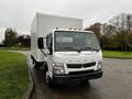 A white 2012 Mitsubishi Fuso FE truck with a large box cargo area and orange roof lights parked on a street