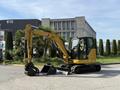 A yellow 2022 Caterpillar 306 excavator with a bucket attachment is positioned on a paved surface, showcasing its hydraulic arm and tracked wheels