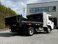 A 2015 Mitsubishi Fuso FE dump truck with a black bed and silver chassis positioned at an angle showing its rear and side view