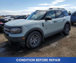 A 2023 Ford Bronco Sport with a light gray exterior and rugged design features is parked in a lot with visible dirt on the lower part of the vehicle