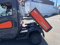 A 2014 Kubota X1100C utility vehicle with an orange and black color scheme featuring a cargo bed tilted up for loading or unloading