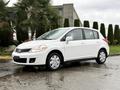 A 2012 Nissan Versa in white with a hatchback design and alloy wheels parked on a wet surface