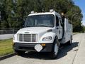 A white 2004 Freightliner M2 truck with a prominent grille and large front bumper featuring a diamond plate accent and side compartments for equipment