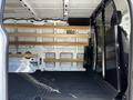 Interior of a 2023 Ford Transit van with wooden shelves along the sides and a metal partition separating the front cabin from the cargo area