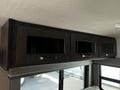 A series of three dark wooden cabinets with glass fronts above a seating area in a 2021 Grand Design Recreational 311BHS camper