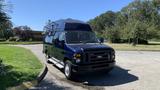 A dark blue 2013 Ford Econoline van with a raised roof and roof rack, positioned at an angle on a driveway