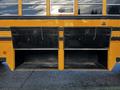 A 2005 Blue Bird 48 passenger bus with two open storage compartments in the lower section of the yellow exterior