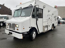 A white 2012 Workhorse W62 delivery truck with multiple side compartments and large front windows parked on a wet surface.