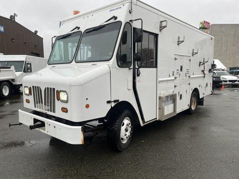 A white 2012 Workhorse W62 delivery truck with multiple side compartments and large front windows parked on a wet surface.