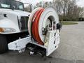 A white 2016 Peterbilt 348 with a large hose reel mounted on the back featuring orange hoses and a control panel with gauges and valves