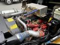 A 2015 Spartan School Bus engine with various colorful hoses and pipes connecting to a metallic compartment and multiple components visible within the engine bay