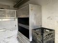 A metallic storage compartment with a mesh front and two black shelves inside, next to a black plastic crate