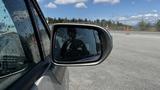 A 2006 Honda Fit with a side mirror reflecting a shadow and droplets of water on its surface