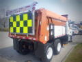 A 2016 International WorkStar 7500 dump truck with an orange and reflective yellow striped tailgate and large black and yellow checkerboard pattern on the back