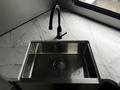 A stainless steel sink with a modern black faucet sits on a smooth marble countertop