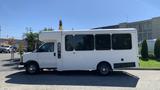 A 2011 Chevrolet Express white shuttle bus with large windows and a raised roof parked on a concrete surface