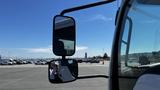 A 2006 Ford LCF 550 showing its side mirrors with a reflection of a person and parked vehicles visible in the mirror