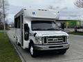 A white 2016 Ford Econoline bus with a ramp for accessibility parked on a street with a clear view of its front and side
