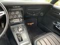Interior of a 1972 Chevrolet Corvette featuring a gear shifter dashboard with dials and controls a black leather seat and a floormat with the Corvette logo