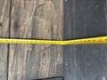 A close-up view of a measuring tape laid flat on a wooden surface with markings showing measurements in inches