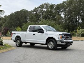 A 2018 Ford F-150 parked with a white exterior and chrome accents featuring a four-door cab and all-terrain tires