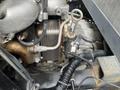 A close-up view of the engine components of a 2008 Mitsubishi Fuso FE180 showing pipes wires and a metal housing