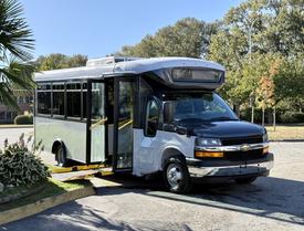 2019 Chevrolet Express bus with an accessible ramp extended and doors open showcasing a two-tone exterior with a black front and silver body