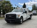 A 2015 Ford F-350 Super Duty truck in white with a flatbed and additional equipment mounted on the roof