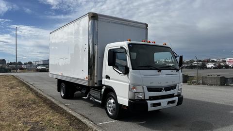 A white 2018 Mitsubishi Fuso FE truck with a large cargo box attached to the back parked on a paved surface