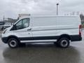 A 2018 Ford Transit van in white with a black stripe along the lower part and silver wheels parked on a wet surface viewed from the side