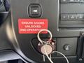 A 2020 Chevrolet Express dashboard with a key in the ignition and a red sign that reads "ENSURE DOORS UNLOCKED AND OPERATIONAL" near the radio controls and switches