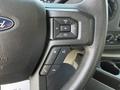 Close-up of the steering wheel controls of a 2023 Ford E-450 showing buttons for volume and phone connectivity